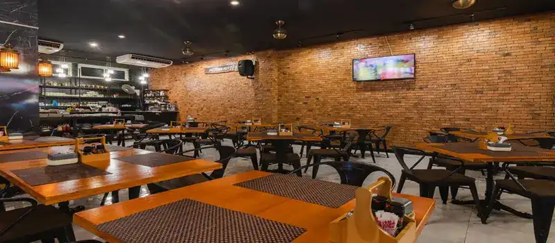 Wooden tables and black metal chairs along a long brick wall inside Pizzeria Hut 1