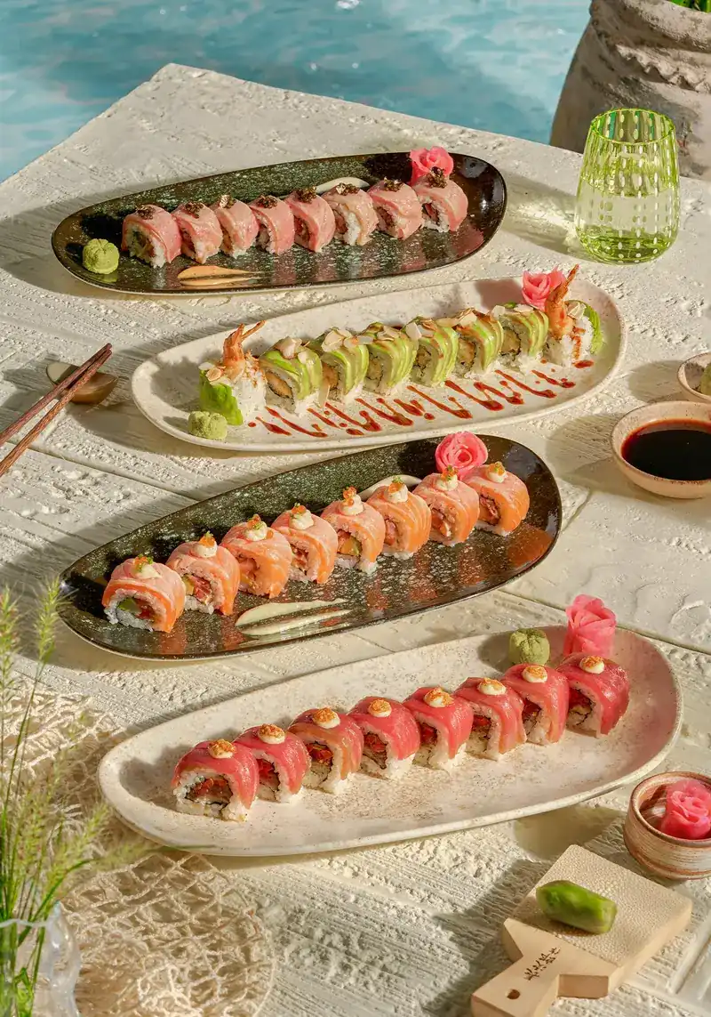 Four plates of sushi rolls on a white table beside the pool