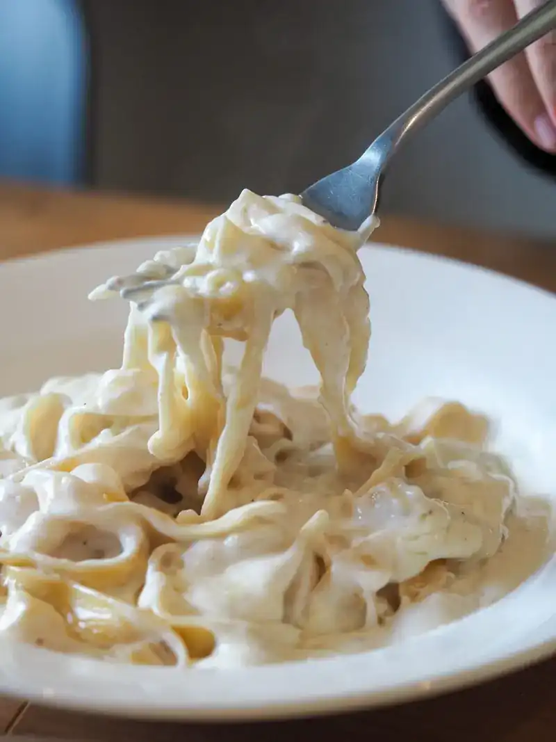 A fork lifting ribbon pasta in a white cream sauce