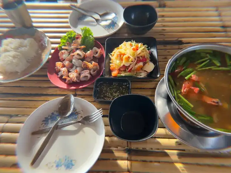 Seen from above: rice, grilled squid, papaya salad and a pot of soup on a bamboo table