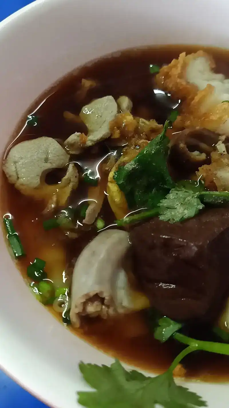 A bowl of dark brown broth with crispy pork, pork offal and coriander