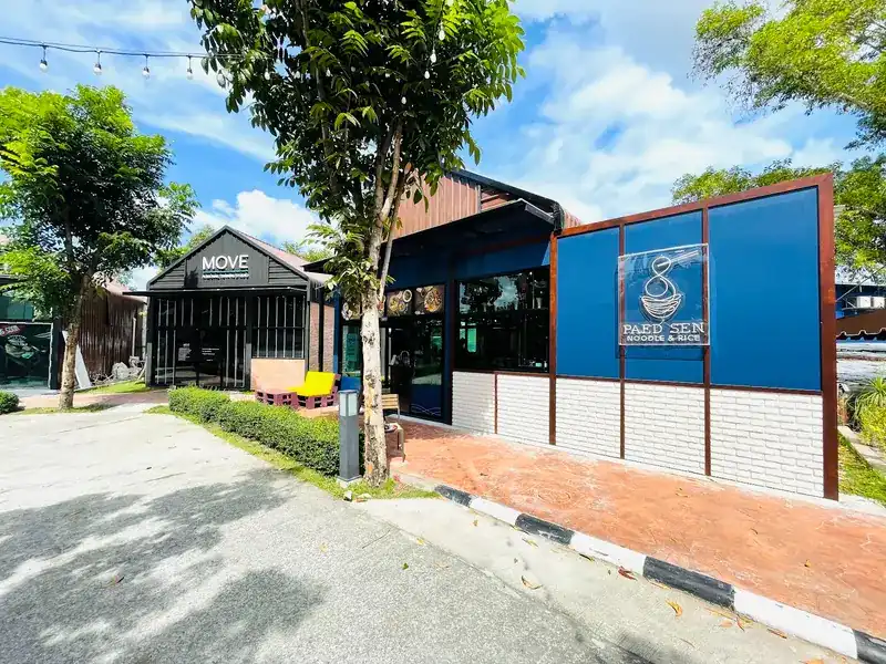 The Paed Sen shop in daylight: blue walls with the bowl logo, a tree and the walkway of Green Plaza Zone