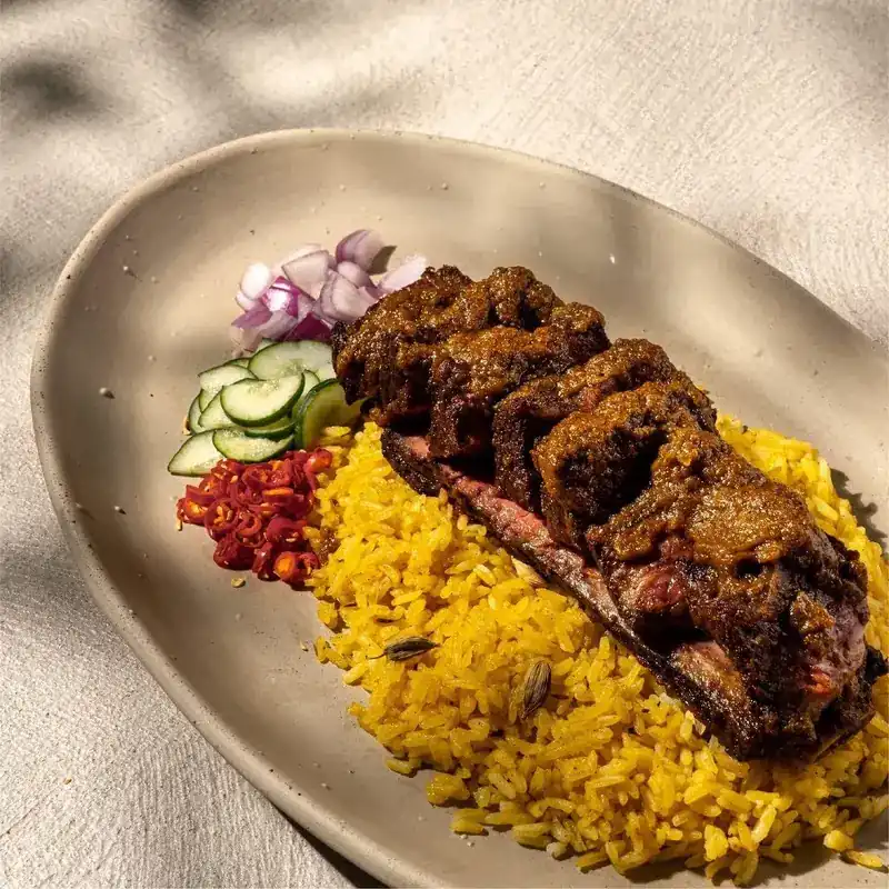 Ribs under a thick, dark sauce on yellow rice, with cucumber, red onion and chopped chilli