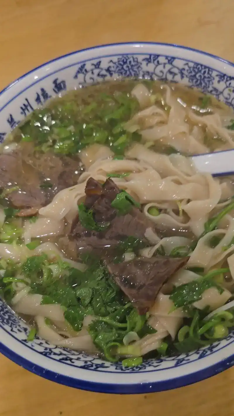 Wide flat noodles in beef broth with beef slices and greens