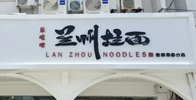 The shop sign, LAN ZHOU NOODLES in red and black above white arches