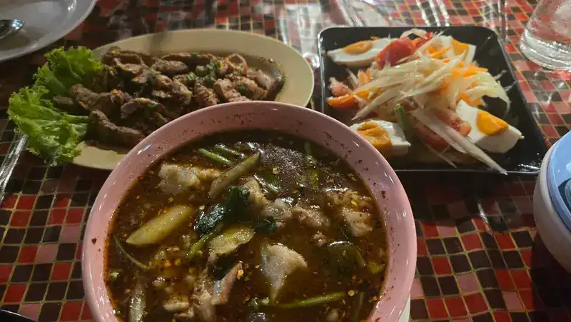 Grilled meat on lettuce, a bowl of spicy soup and papaya salad with salted egg