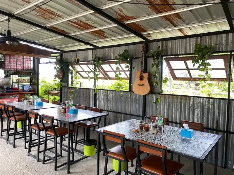 Open-sided dining room under a corrugated tin roof, with tiled tables, hanging plants and a guitar on the wall