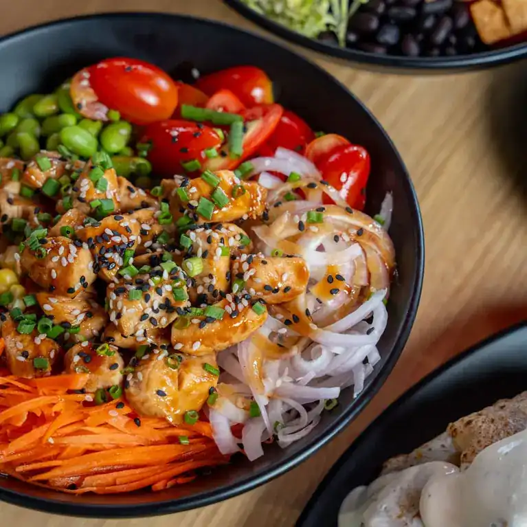 Bowl of glazed chicken with sesame, cherry tomatoes, edamame, carrot and onion