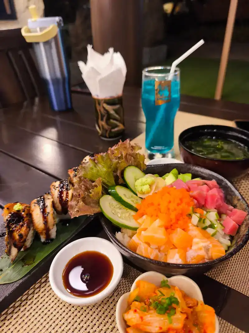 A rice bowl topped with salmon, tuna, fish roe and cucumber, with a seared sushi roll and miso soup