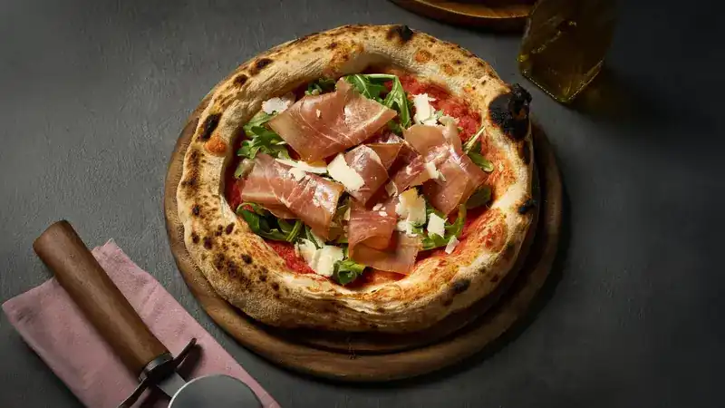 Neapolitan pizza with Parma ham, rocket and shaved Parmesan on a wooden board