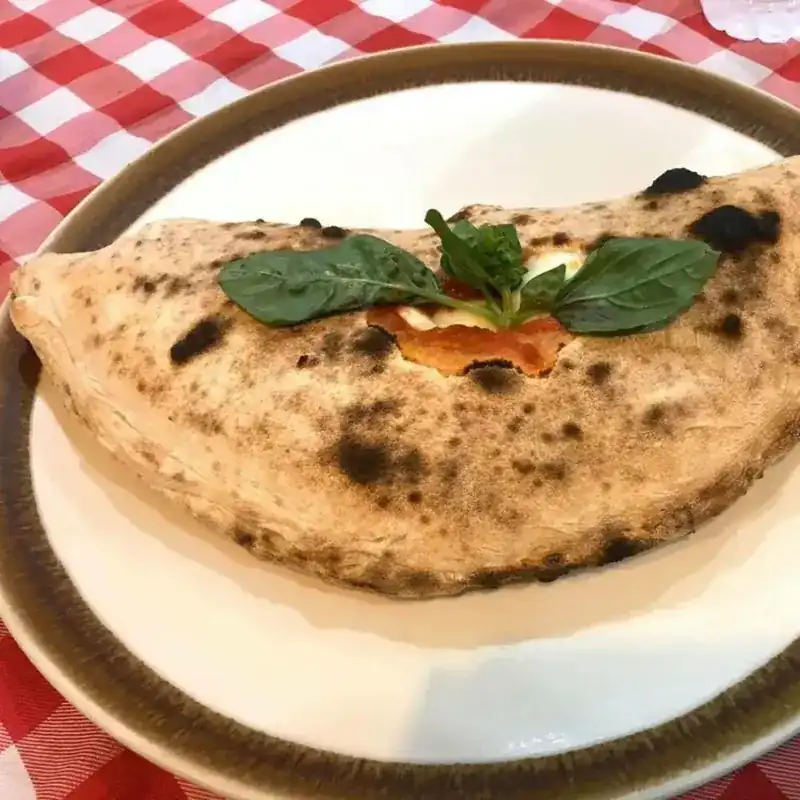 A calzone blistered by the wood oven, topped with basil leaves