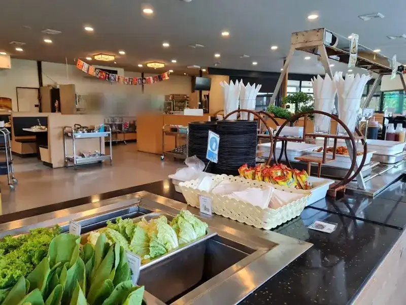 The buffet bar with fresh greens and stacks of plates, the dining room behind