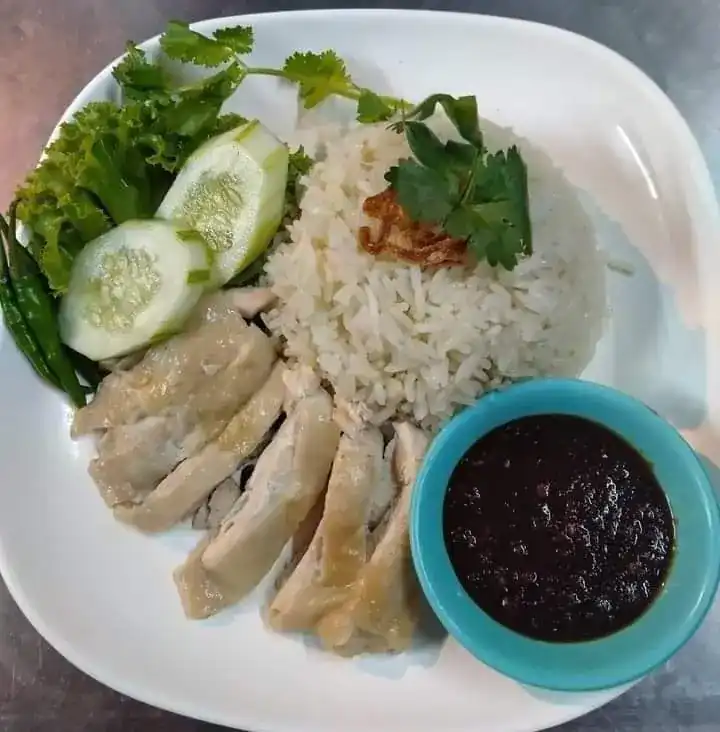 Sliced boiled chicken on rice with cucumber, greens and a small bowl of dark dipping sauce