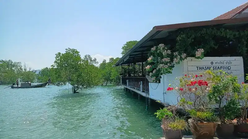 The restaurant on stilts over the water, its Thasak Seafood sign among flowering pots, a longtail boat by the mangroves