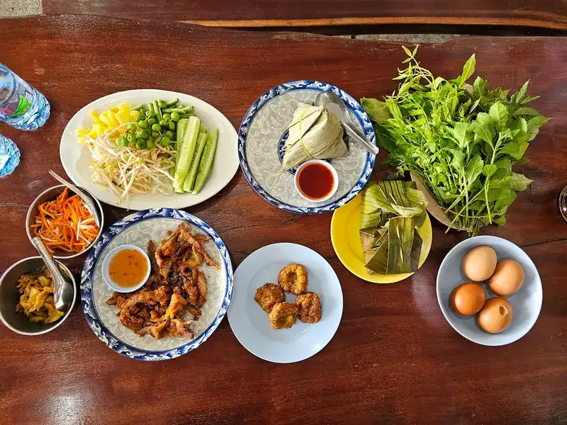 A wooden table set with fried pork, fish cakes, ba chang, eggs and greens