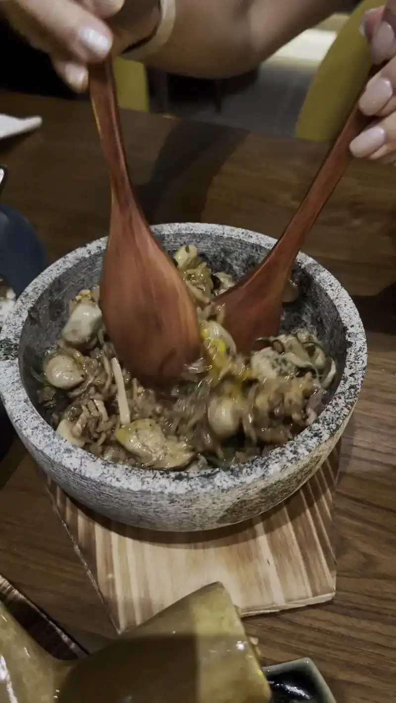 A dish tossed at the table with two wooden spoons in a stone bowl