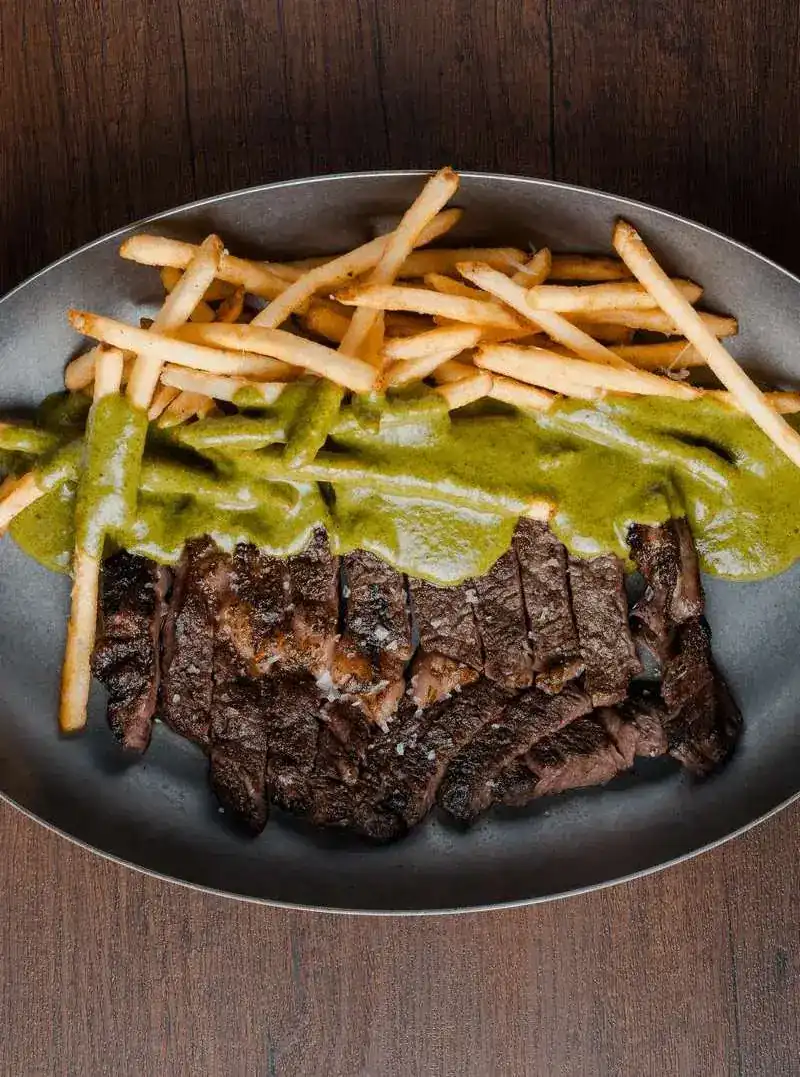 Sliced grilled ribeye under green sauce with thin fries