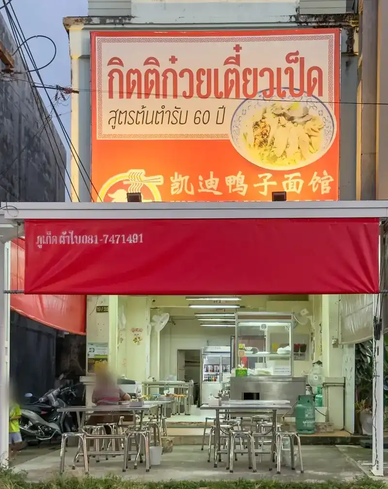 The Manik shop: orange Kitti sign above a red awning, steel tables inside / หน้าร้านสาขาม่าหนิก ป้ายสีส้มของกิตติเหนือกันสาดสีแดง โต๊ะสแตนเลสด้านใน