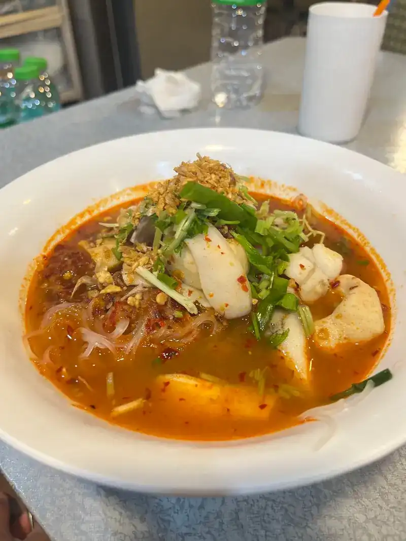 A spicy red dish with glass noodles, topped with fried garlic and spring onion