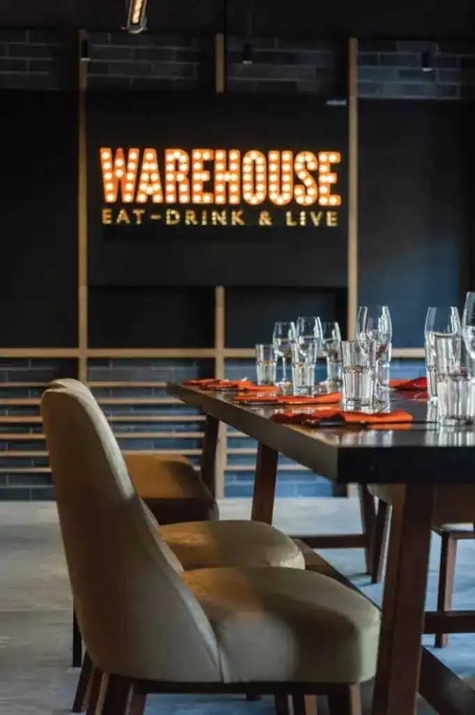The WAREHOUSE bulb sign over a long table set with glasses and orange napkins