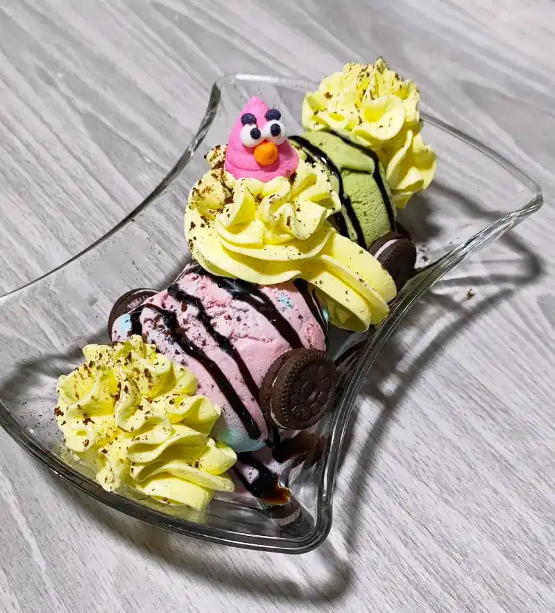 Scoops of ice cream in a glass dish with whipped cream and cookies