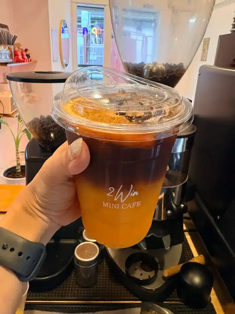 An iced espresso orange in a 2Win cup, held up at the coffee machine