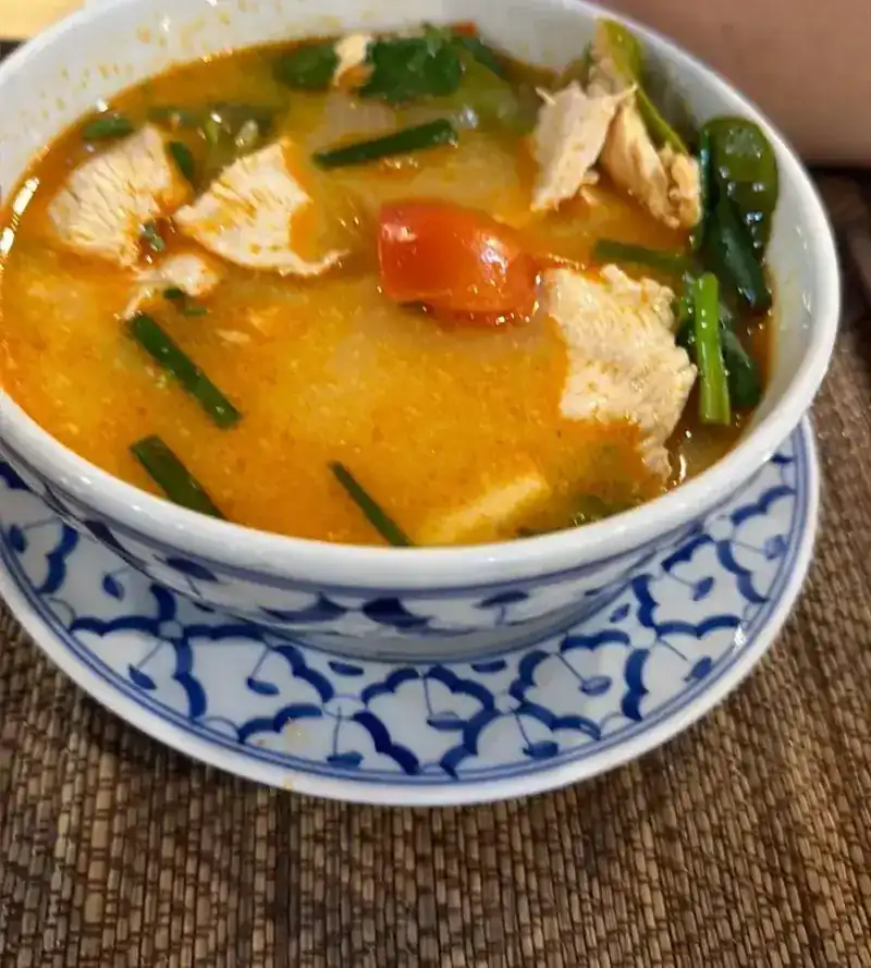A bowl of tom yum with chicken on a blue and white saucer / ต้มยำไก่ในชามลายครามสีน้ำเงินขาว