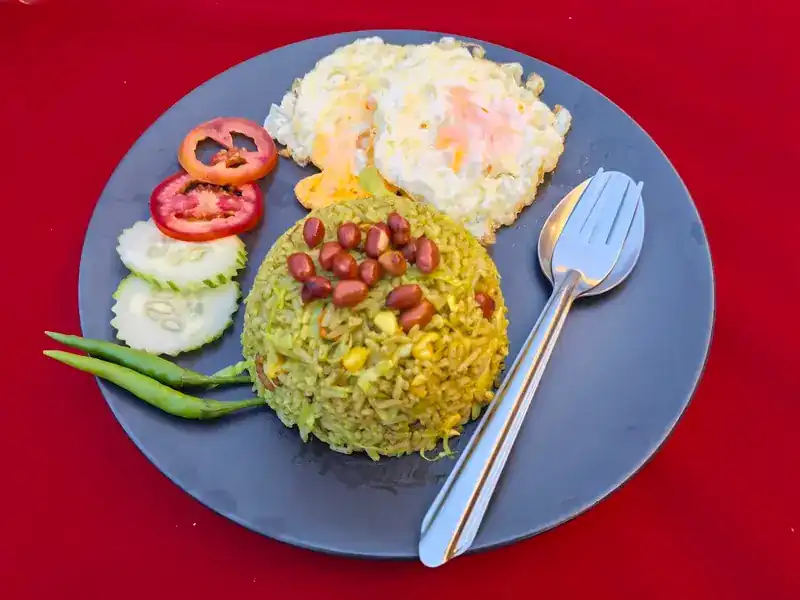 Fried rice topped with peanuts, two fried eggs, cucumber, tomato and green chillies, on a red cloth