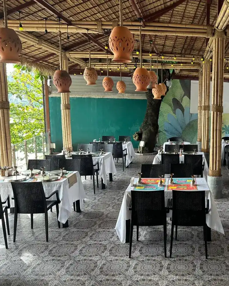 Open-air dining room with bamboo pillars, hanging clay lamps and tables laid with white cloths