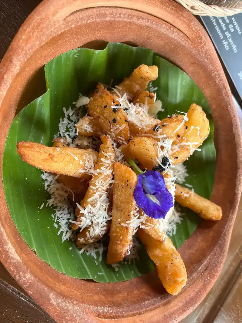 Fries under grated cheese on a banana leaf in a clay bowl, with a blue butterfly pea flower