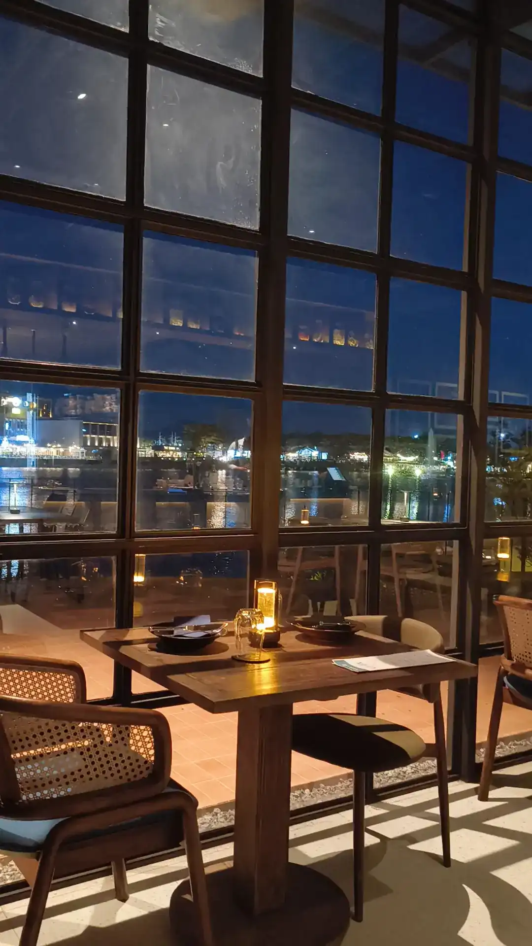 Window tables at night, candlelight on the table and lights across the water