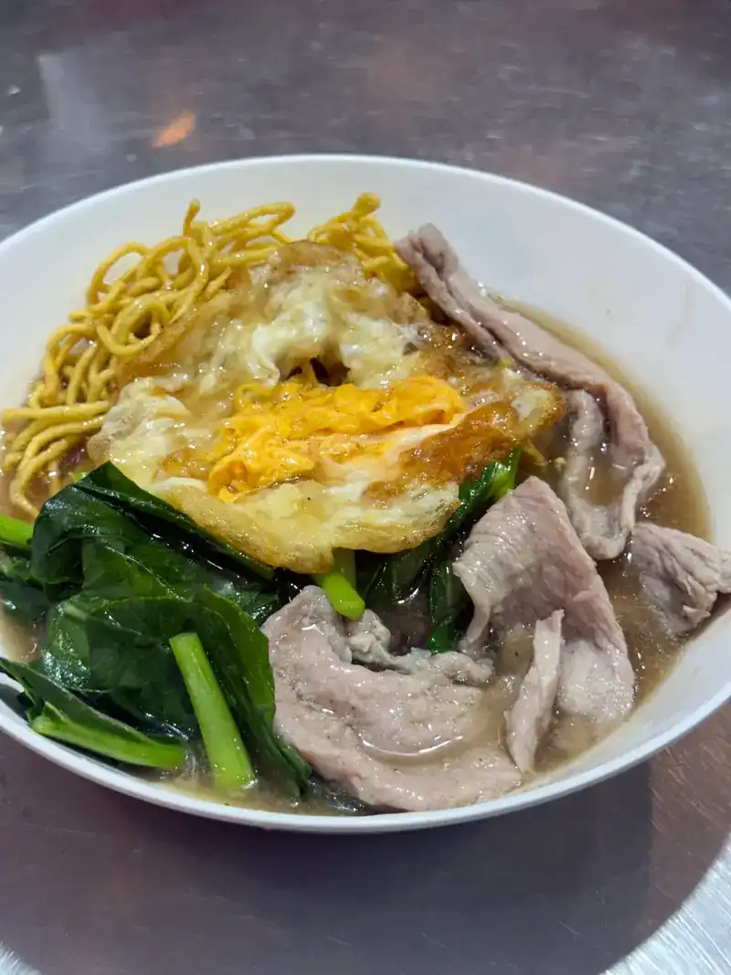 A bowl with a fried egg, crispy noodles, sliced pork and Chinese kale in gravy / ชามไข่ดาว บะหมี่กรอบ หมูสไลซ์ และผักคะน้าในน้ำราด