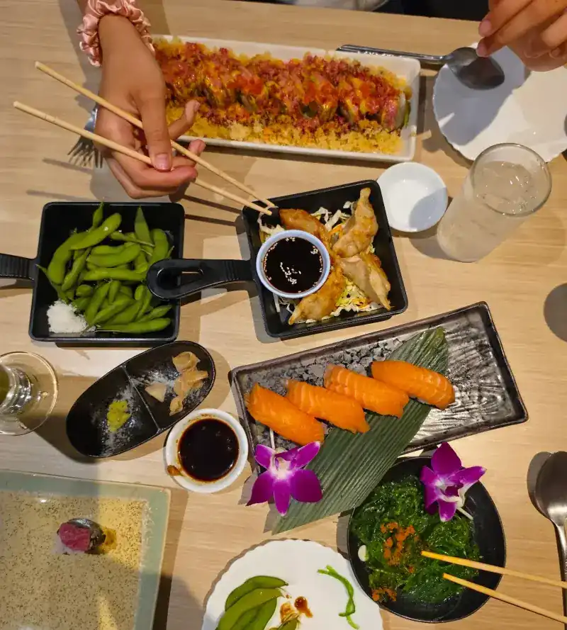 A table seen from above with salmon nigiri, gyoza, edamame, seaweed salad and a topped roll