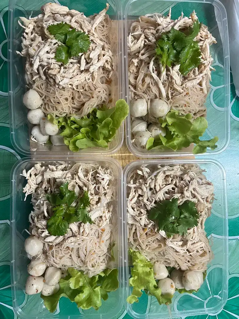 Four takeaway boxes of thin rice noodles topped with shredded chicken, coriander, meatballs and lettuce