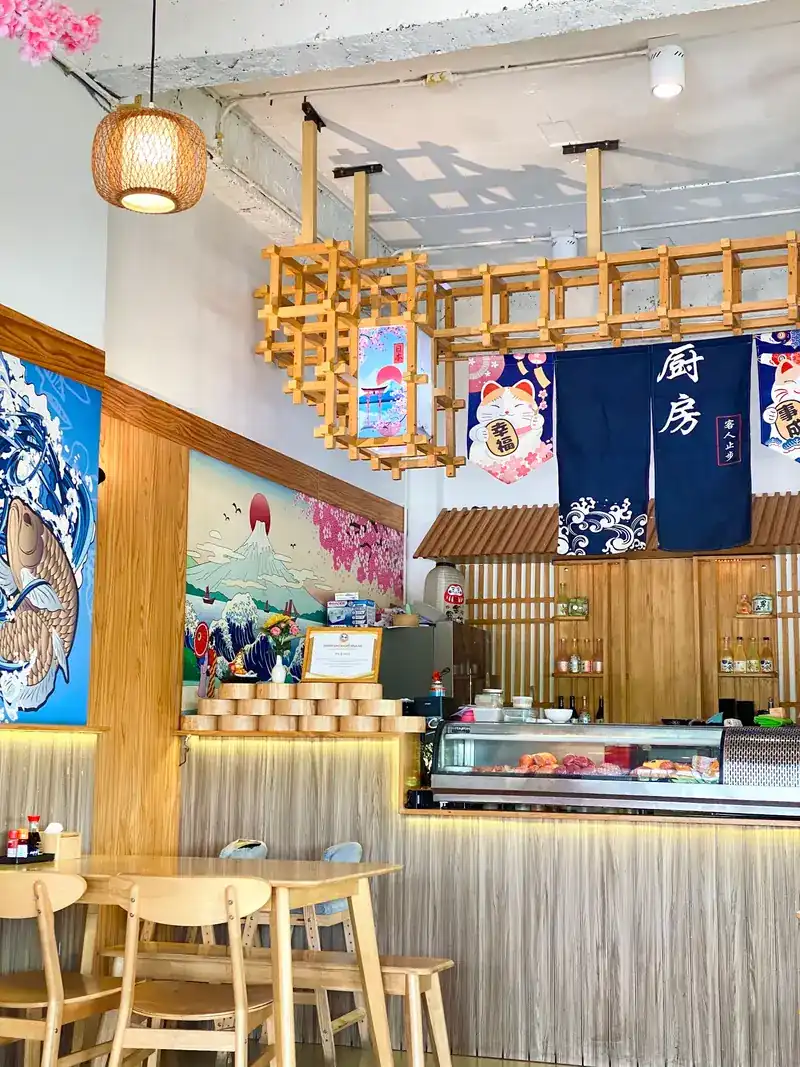 Haru's dining room: pine tables, a koi and wave mural, Mount Fuji with cherry blossom, and the sushi counter under an indigo noren
