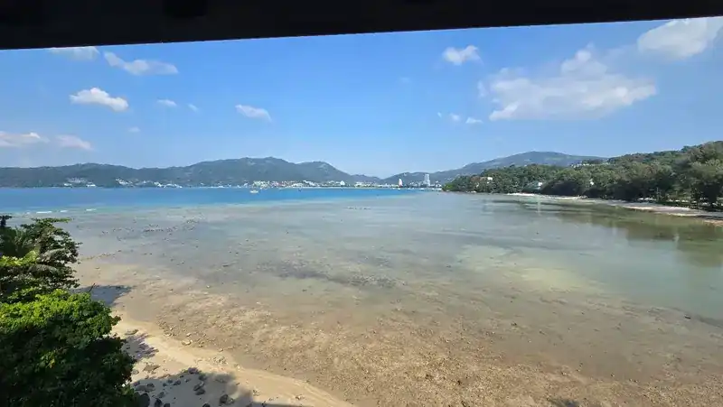 Low tide: wet sand and shallow water below the restaurant, hills along the far shore.