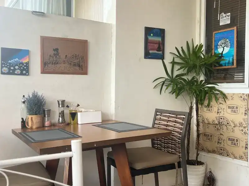 Inside: a wooden table set with place mats and a pot of lavender, paintings on white walls and a tall plant