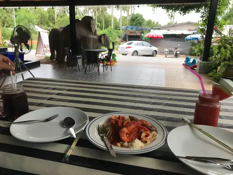 A terrace table with seafood spaghetti and a red fruit shake, the elephant statues beyond