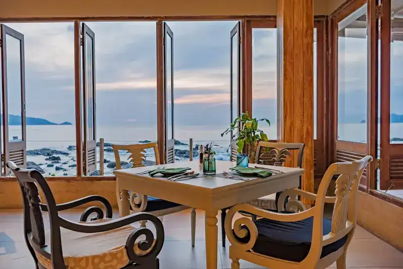 Dining room with tall wooden windows open to the sea