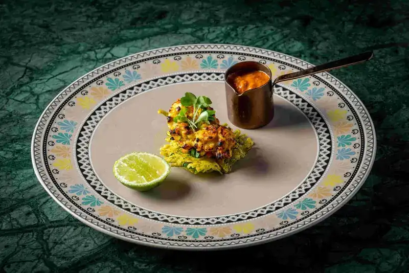Grilled slipper lobster on a patterned plate with a small copper pot of sauce and half a lime
