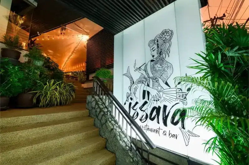 Steps up to the restaurant beside the white Issara sign, with palms on the right