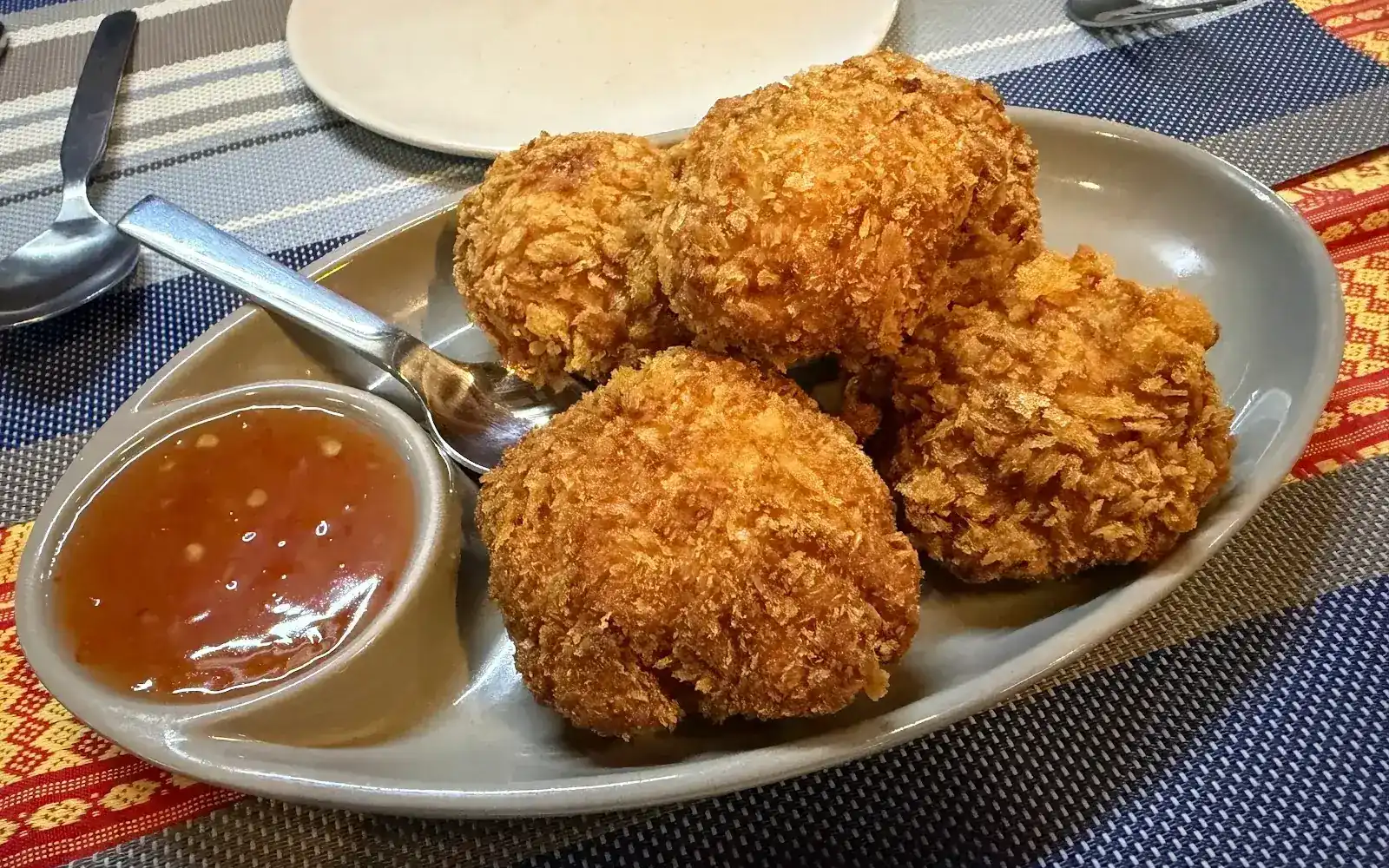 Crisp fried shrimp cakes with a dipping sauce on a woven table runner