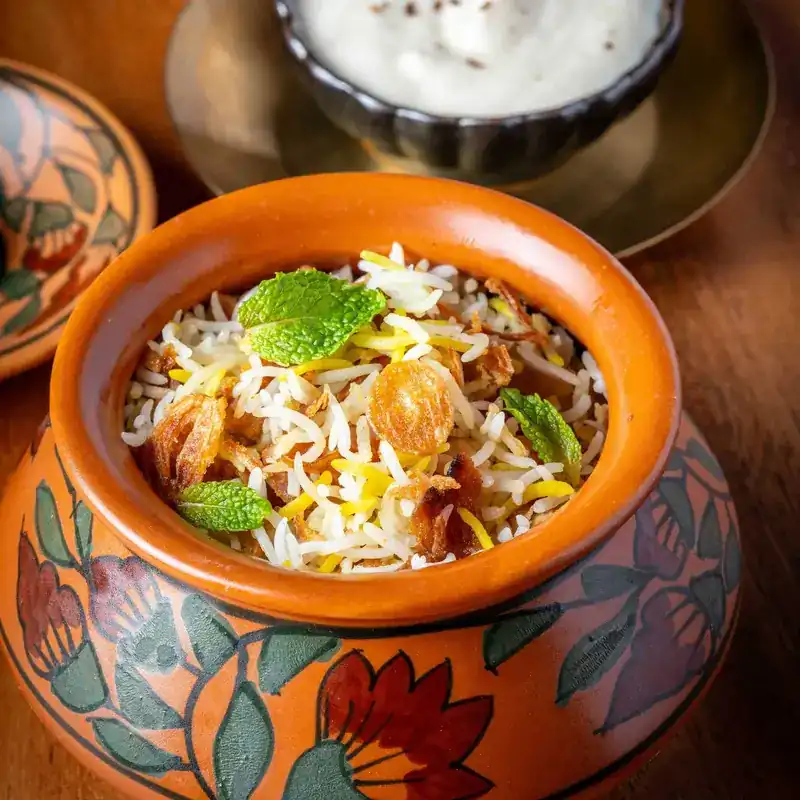 Biryani in a painted clay pot, with mint leaves and fried onions