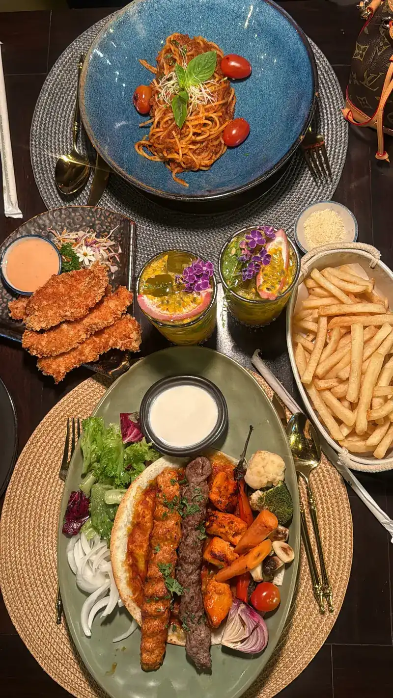 A table seen from above: a kebab platter with salad and bread, fries, fried strips with a dip, pasta with tomatoes and two drinks