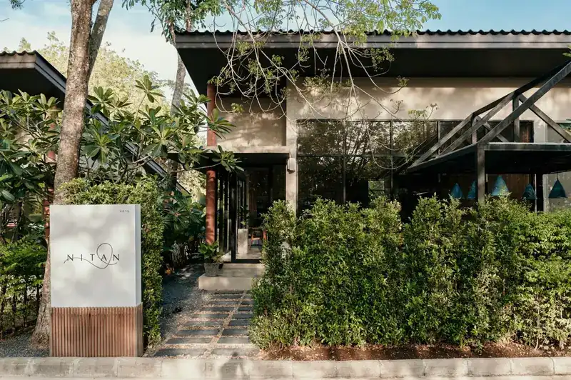 The front of Nitan behind a green hedge, with the white Nitan sign at the path