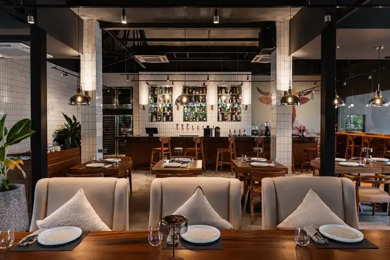 Dining room with a long wooden table, cushioned chairs and the bar behind