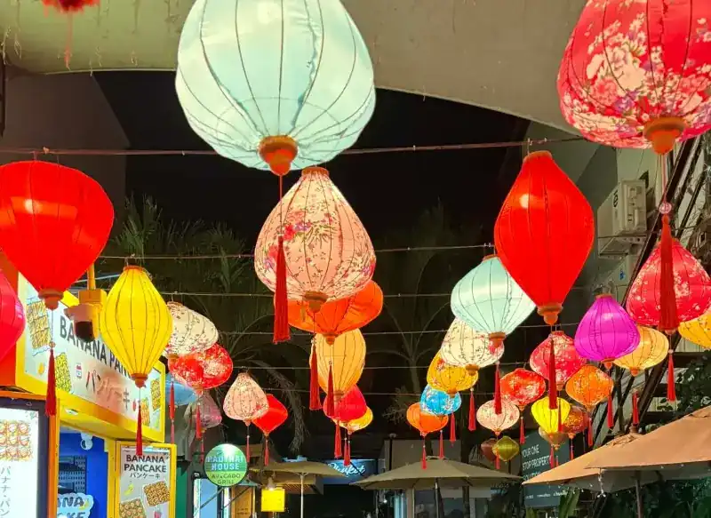 Paper lanterns lit at night over the lane, with the round Padthai House sign below them