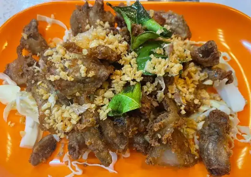Crispy fried pork topped with fried garlic and lime leaves, on shredded cabbage