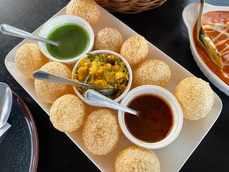 Pani puri with green chutney, spiced potato and a dark sauce