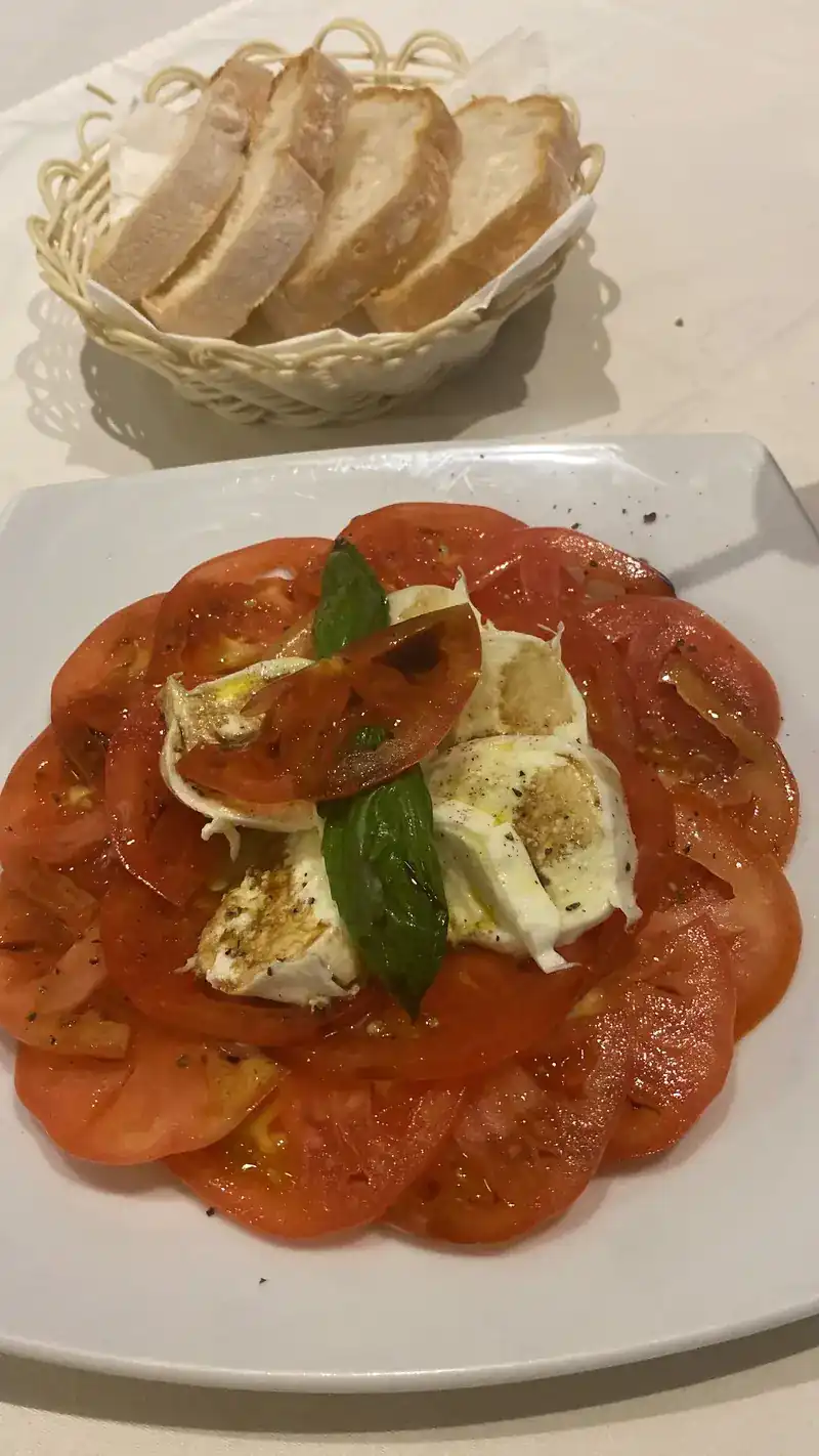 Sliced tomato with mozzarella and basil, and a basket of bread